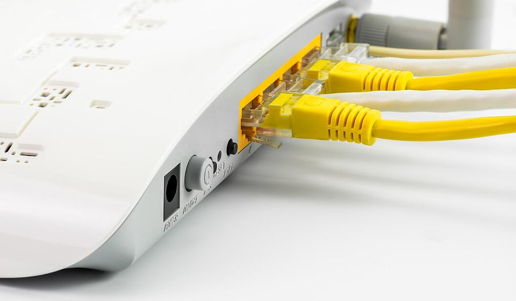 Close-Up der Rückseite eines weißen Routers, in den zwei gelbe Kabel führen. Für eine schnelle Internetverbindung ist der NE4 Ausbau unerlässlich.